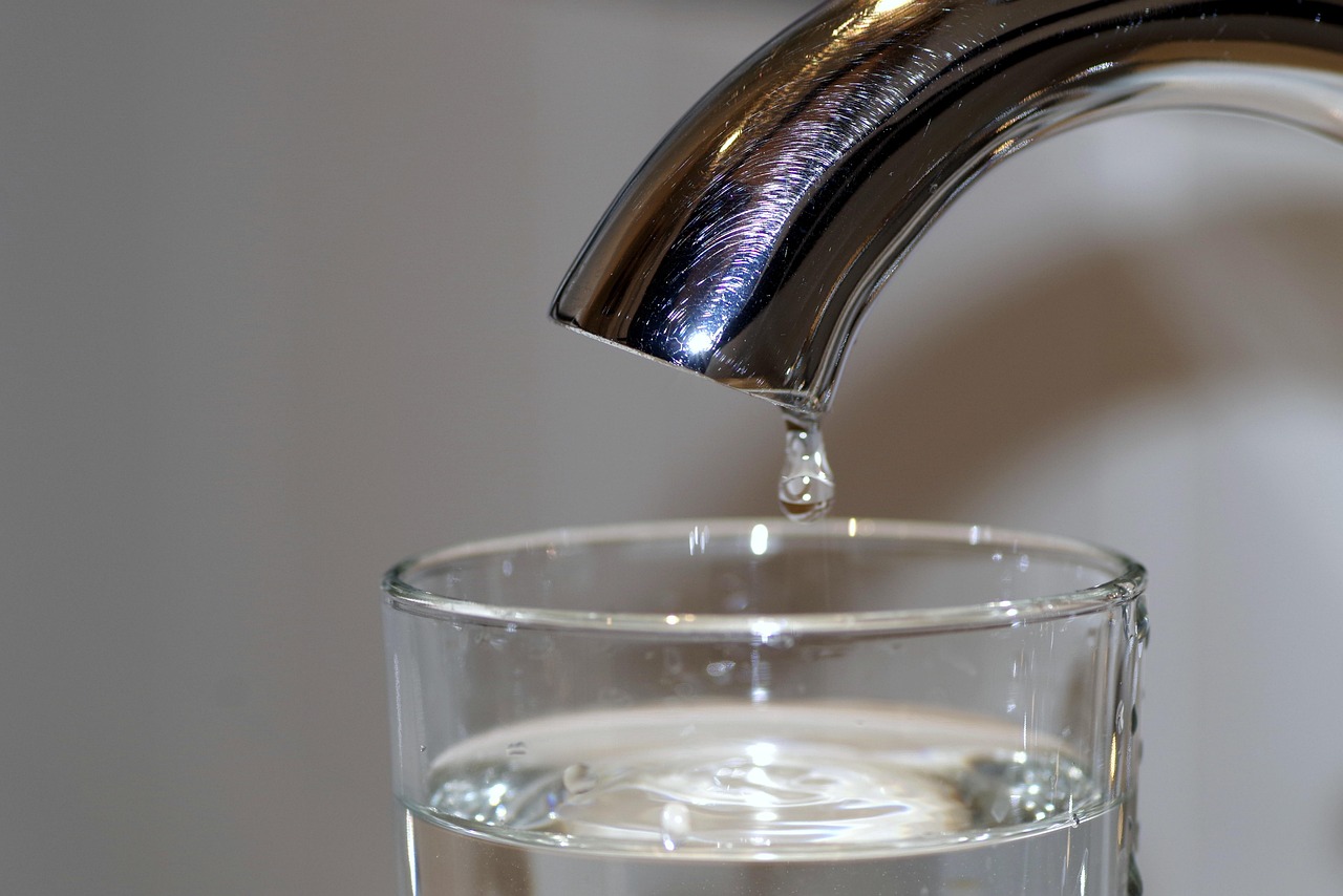 Robinet qui coule au-dessus d'un verre d'eau, symbole du gaspillage sur la facture d'eau